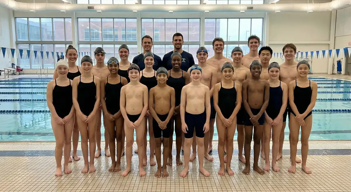 مجموعة سباحين من أعمار مختلفة يقفون بجوار حوض سباحة داخلي مع مدربيهم في Aquagem Swim Academy